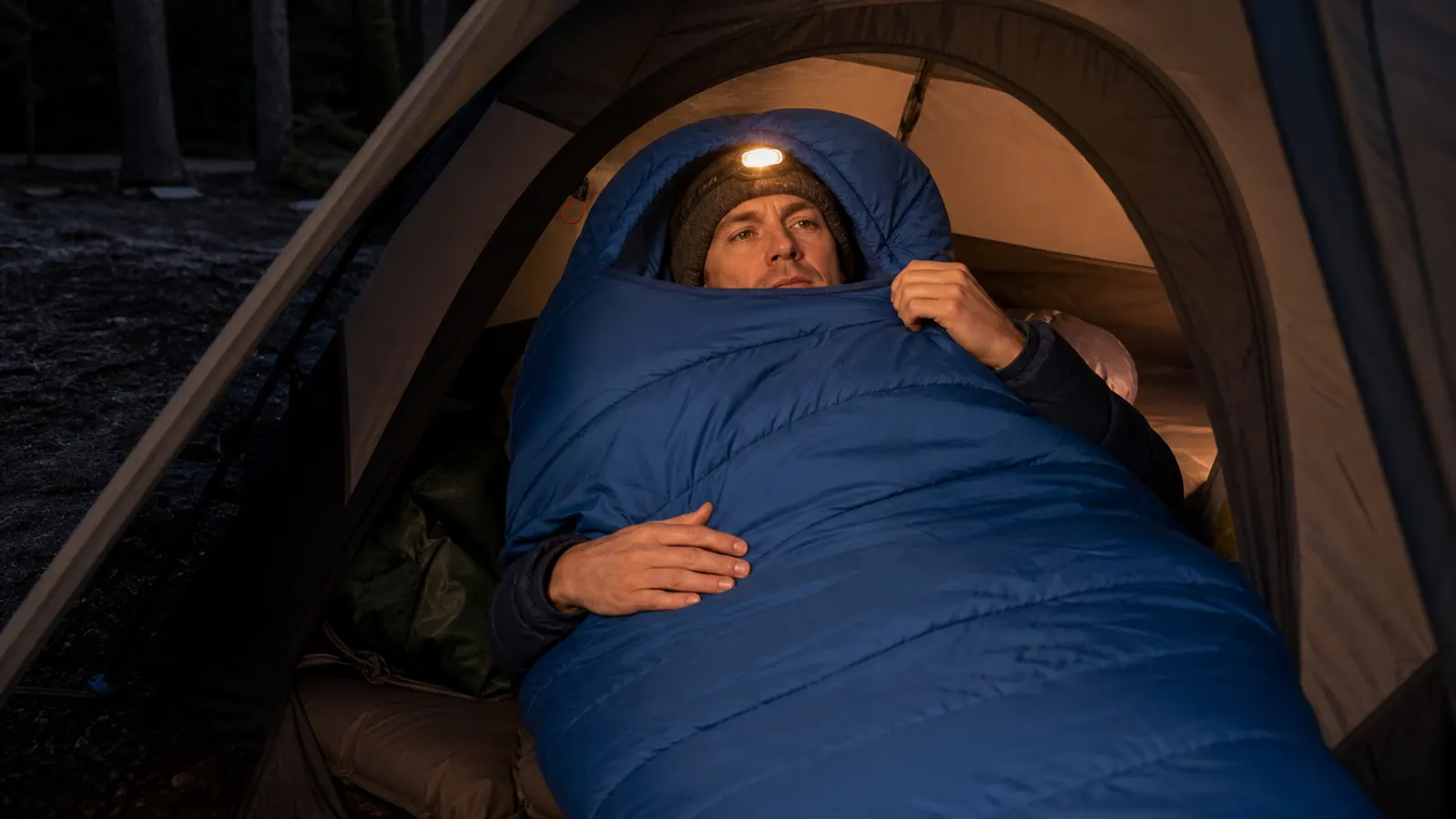 Coleman North Rim mummy sleeping bag laid out on a wooden picnic table at a campsite, zipped fully closed showing the hood