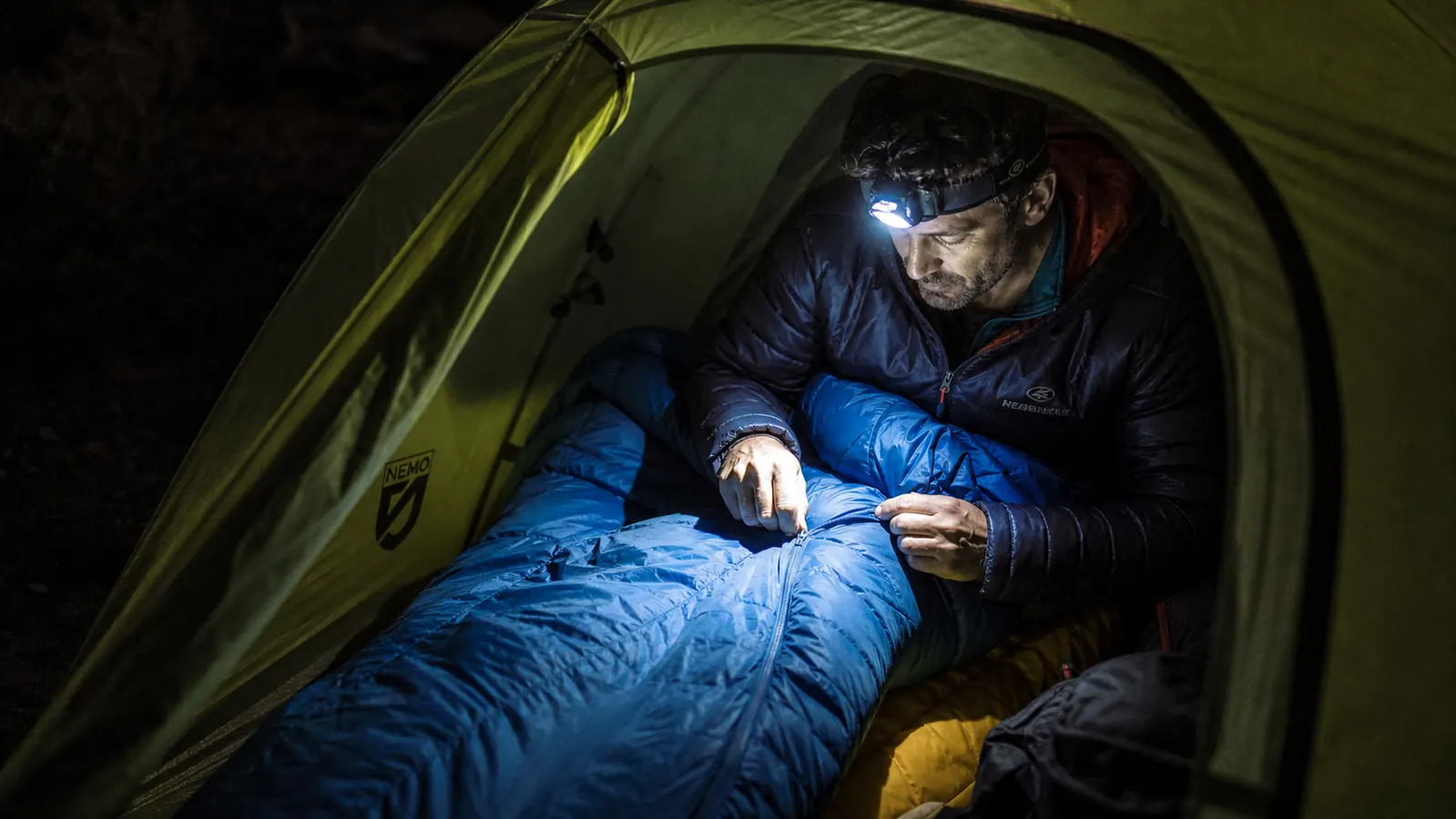 Mummy sleeping bag compressed inside a stuff sack next to a large rectangular bag laid out showing the size difference