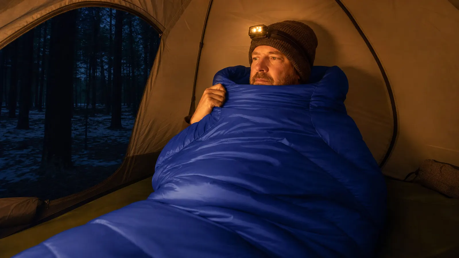 Hands pulling a mummy sleeping bag out of its stuff sack next to a camping pack at a trailhead