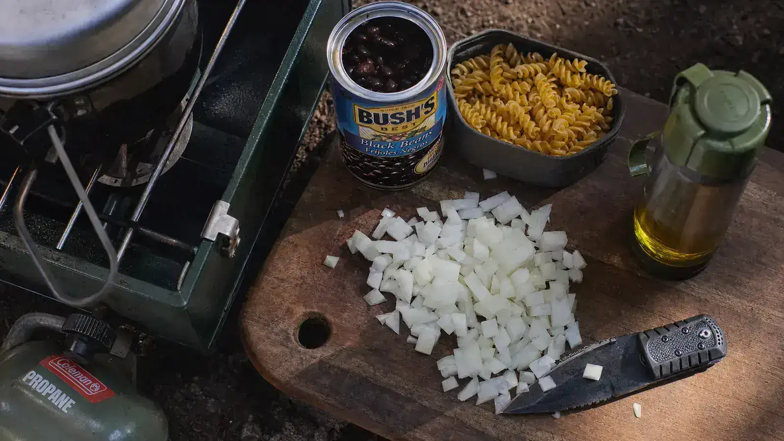 Campsite mise en place setup showing pre-chopped vegetables, spices, and ingredients organized in zip-lock bags beside a stove